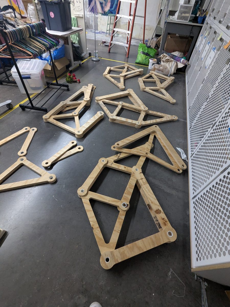 Cut plywood links laid out on the floor with white PVC bushings pressed into the joints